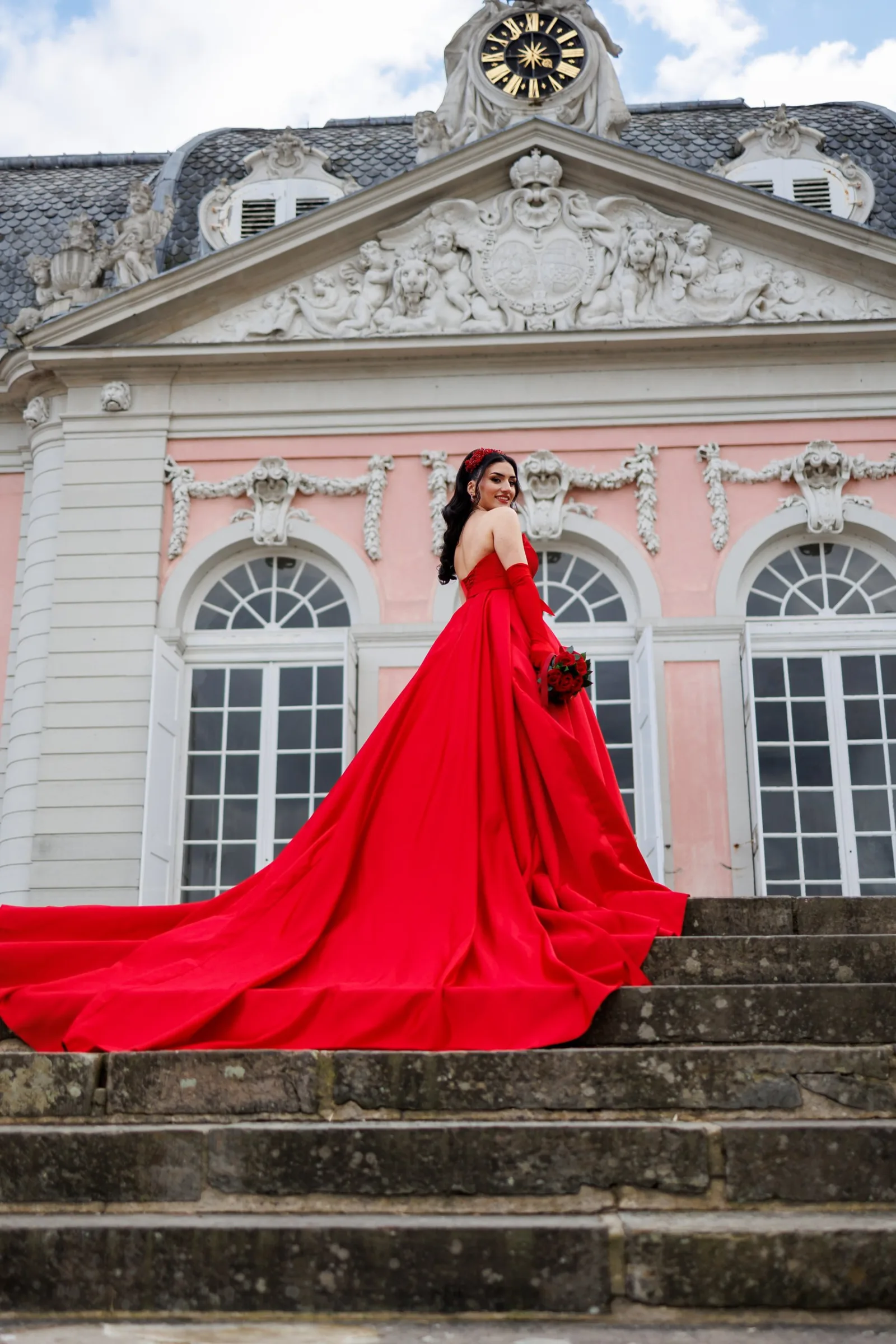Woman in a long red gown on the steps of a palace