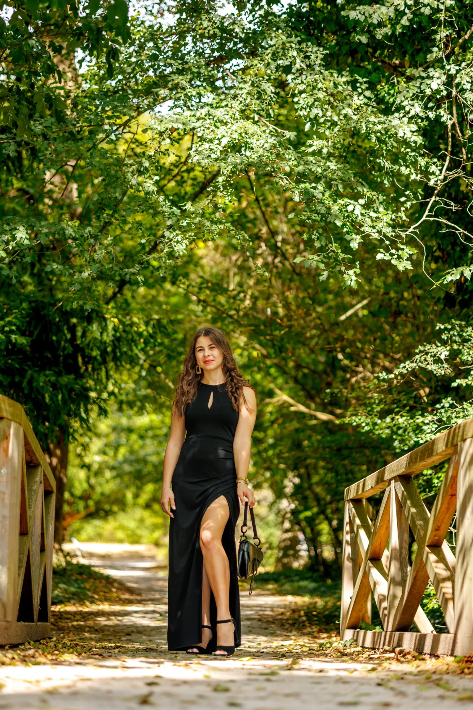 Portrait of a woman in a black dress on a wooden forest bridge